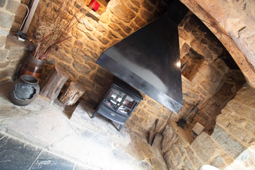 Rustic stone inglenook fireplace and wood-burning stove inside The Indian Queen