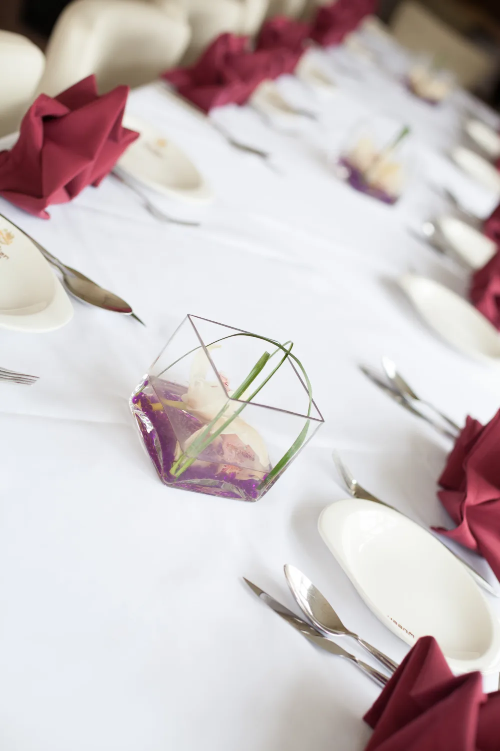 Dining table with burgundy napkin, branded plate and orchid centrepiece